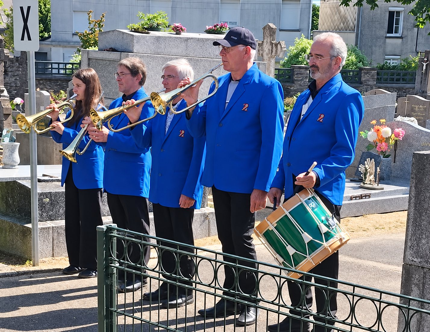 Cinq musiciens en vestes bleues jouent de la trompette et du tambour devant des tombes dans un cimetière.